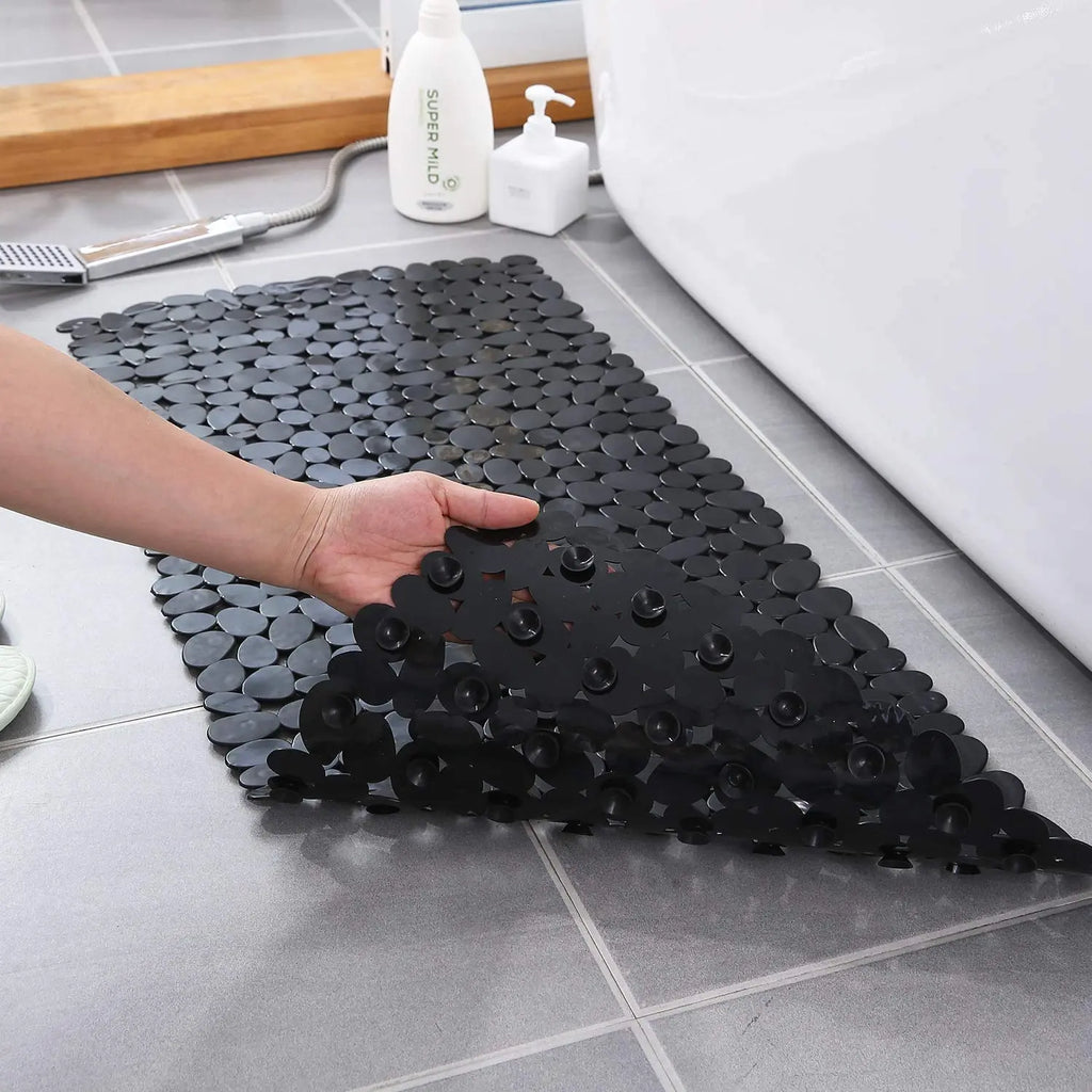 Flexible black stone pebble bath mat showing suction cup underside for floor grip